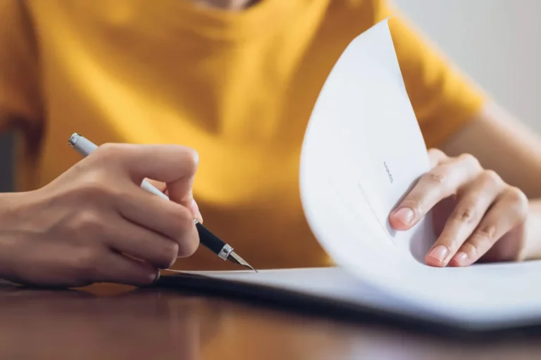 A woman signing a document with a pen.